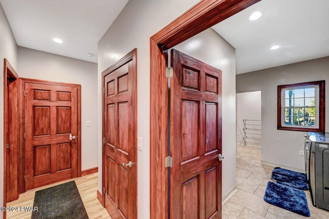 Interior hallway with several wood doors, recessed ceiling lights, and a tiled room visible through an open doorway.