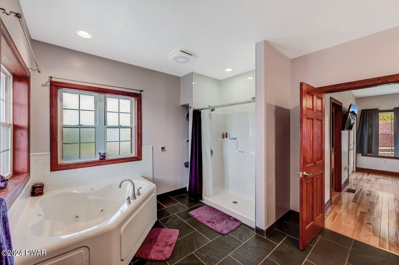 Bathroom with a corner soaking tub, walk-in shower, frosted window, dark tile floor, and an open door leading to a bedroom or hallway.