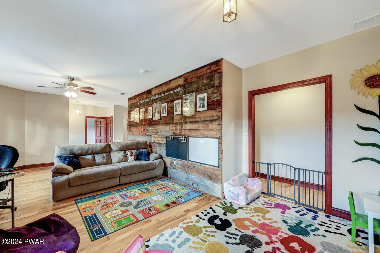 A living room with a brown sofa, colorful rugs, and a rustic wood accent wall with framed photos, open doorway and child gate nearby.