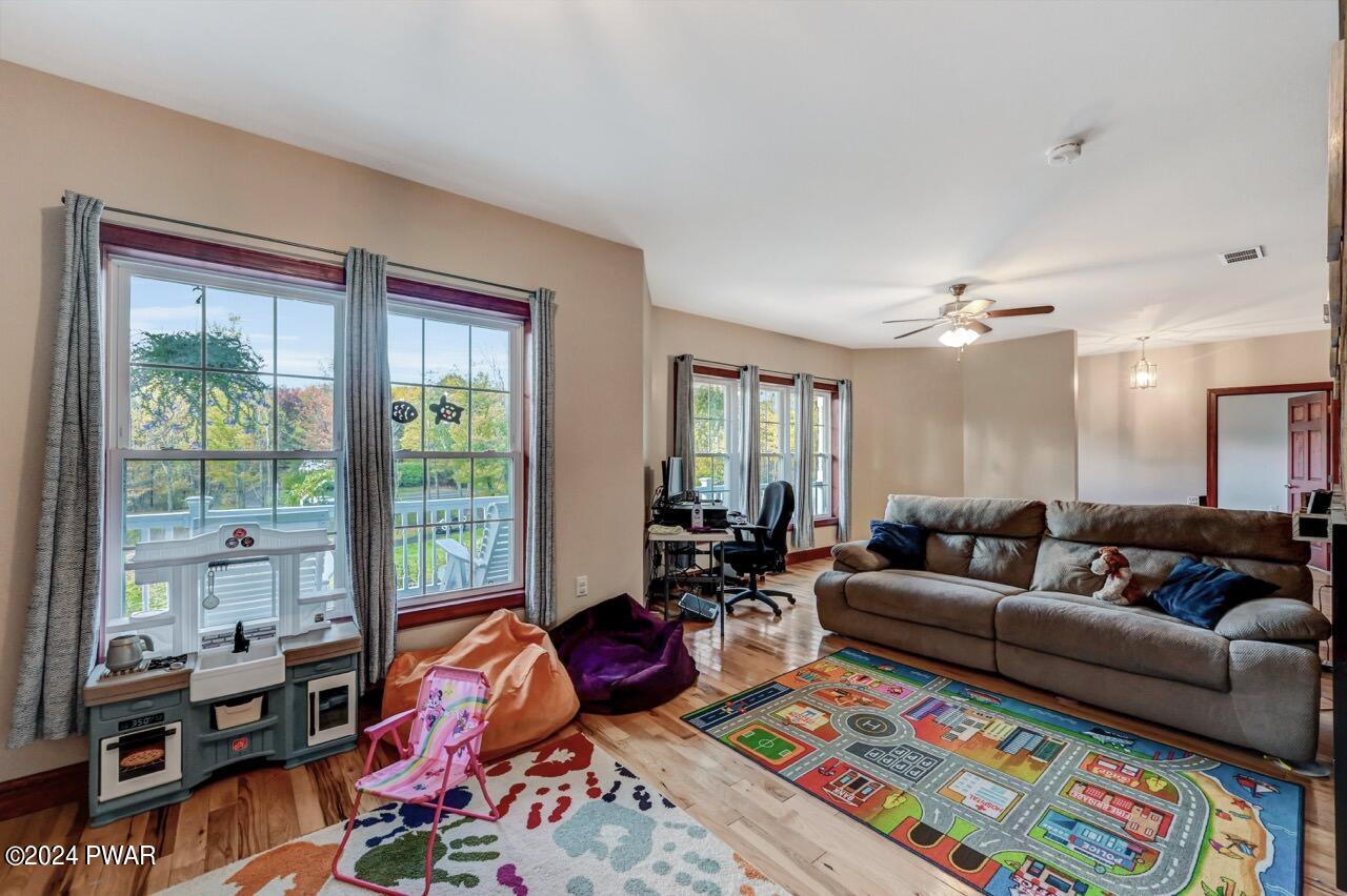 A furnished living room with a large sofa, hardwood floors, multiple windows, and children’s play items.
