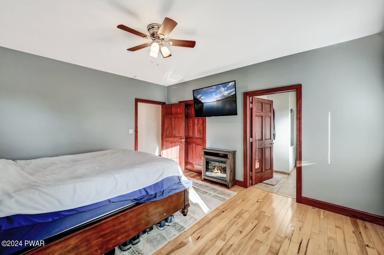 Furnished bedroom with a bed, ceiling fan, wall-mounted television, and a small fireplace heater near the doorway.