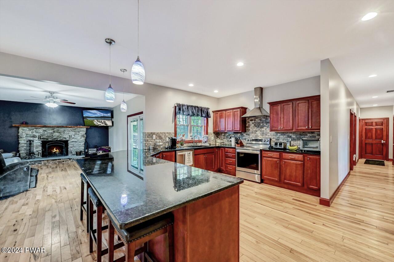 Open-concept kitchen with wood cabinets, granite island, stainless appliances, and a living room with a stone fireplace visible beside it.