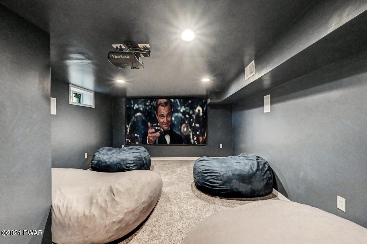 A dark home theater room with a projector on the ceiling, a large screen at the far end, and several beanbag chairs on carpeted flooring.