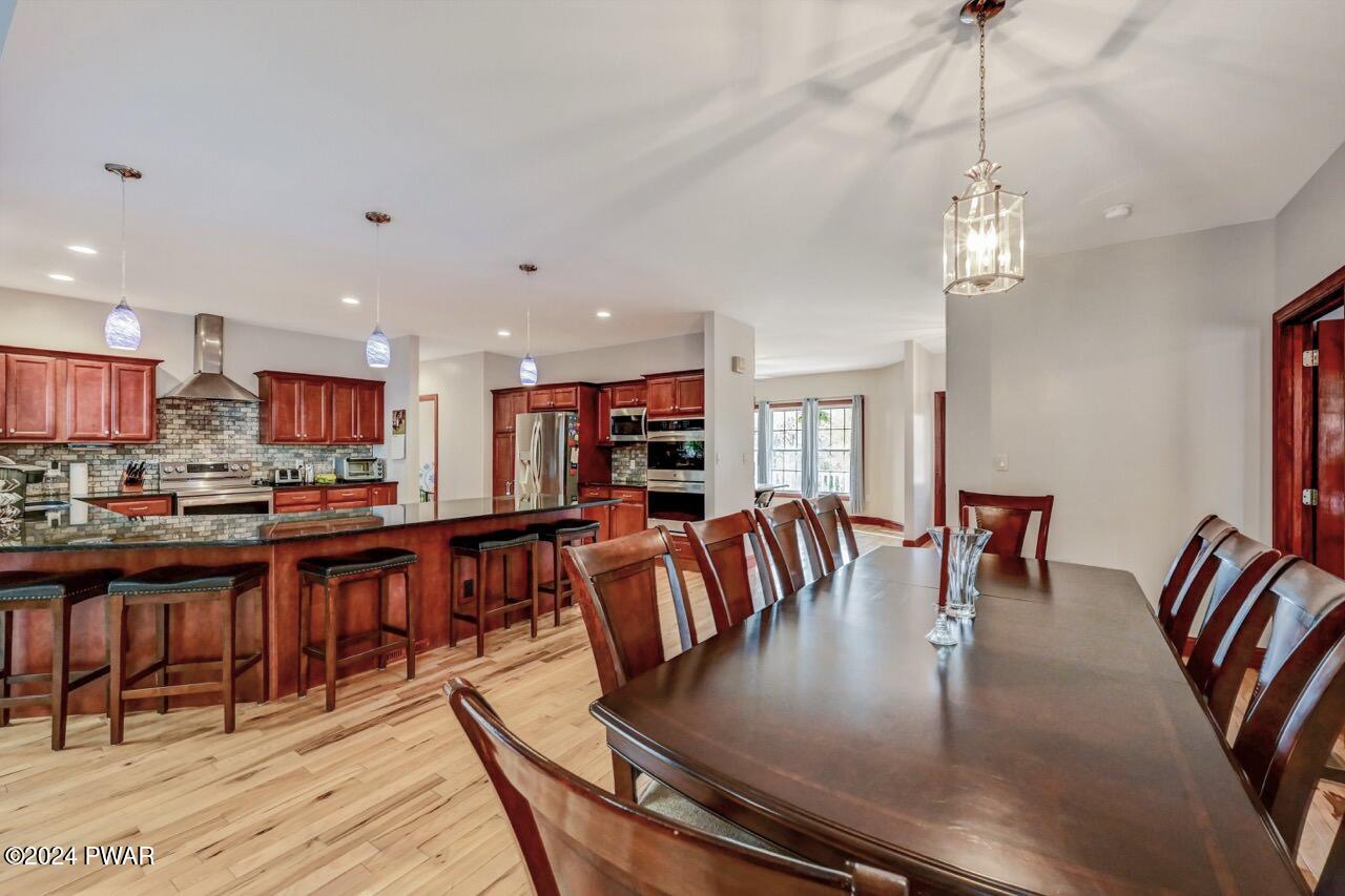Open-concept kitchen with wood cabinets, stainless steel appliances, granite island with bar stools, and a dining table in the foreground.