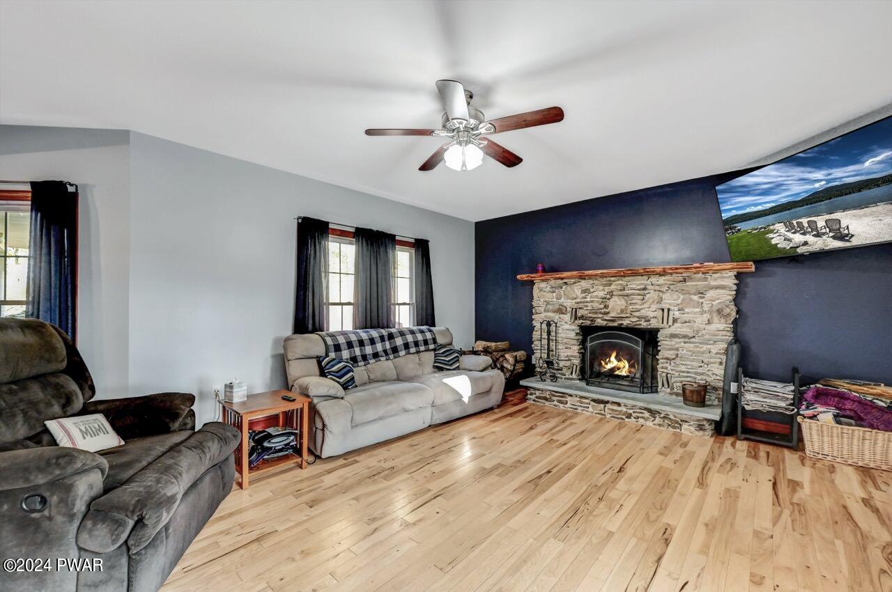 Living room with hardwood floors, ceiling fan, two sofas, and a stone fireplace on a dark accent wall.