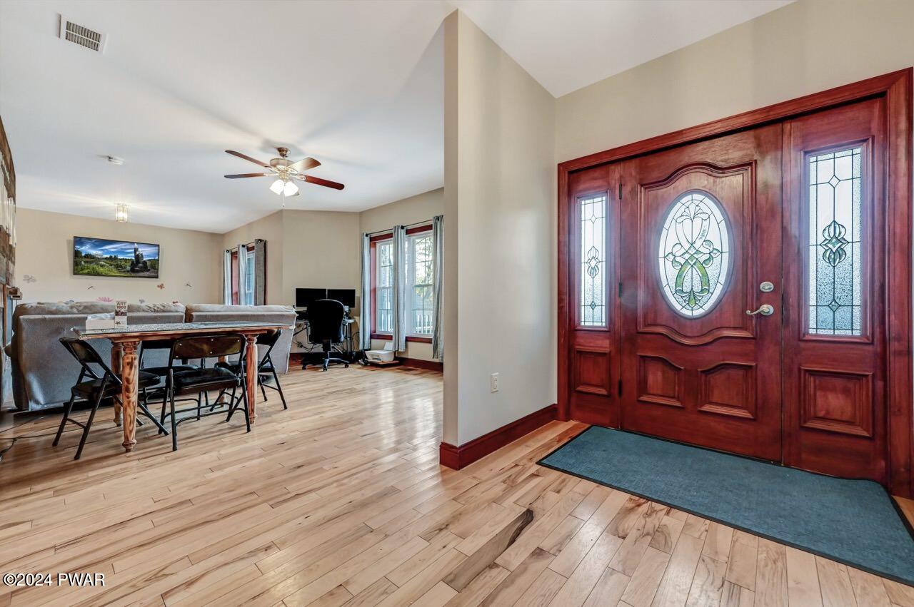 Interior foyer with a decorative wooden front door and adjoining open living/dining space with hardwood floors.