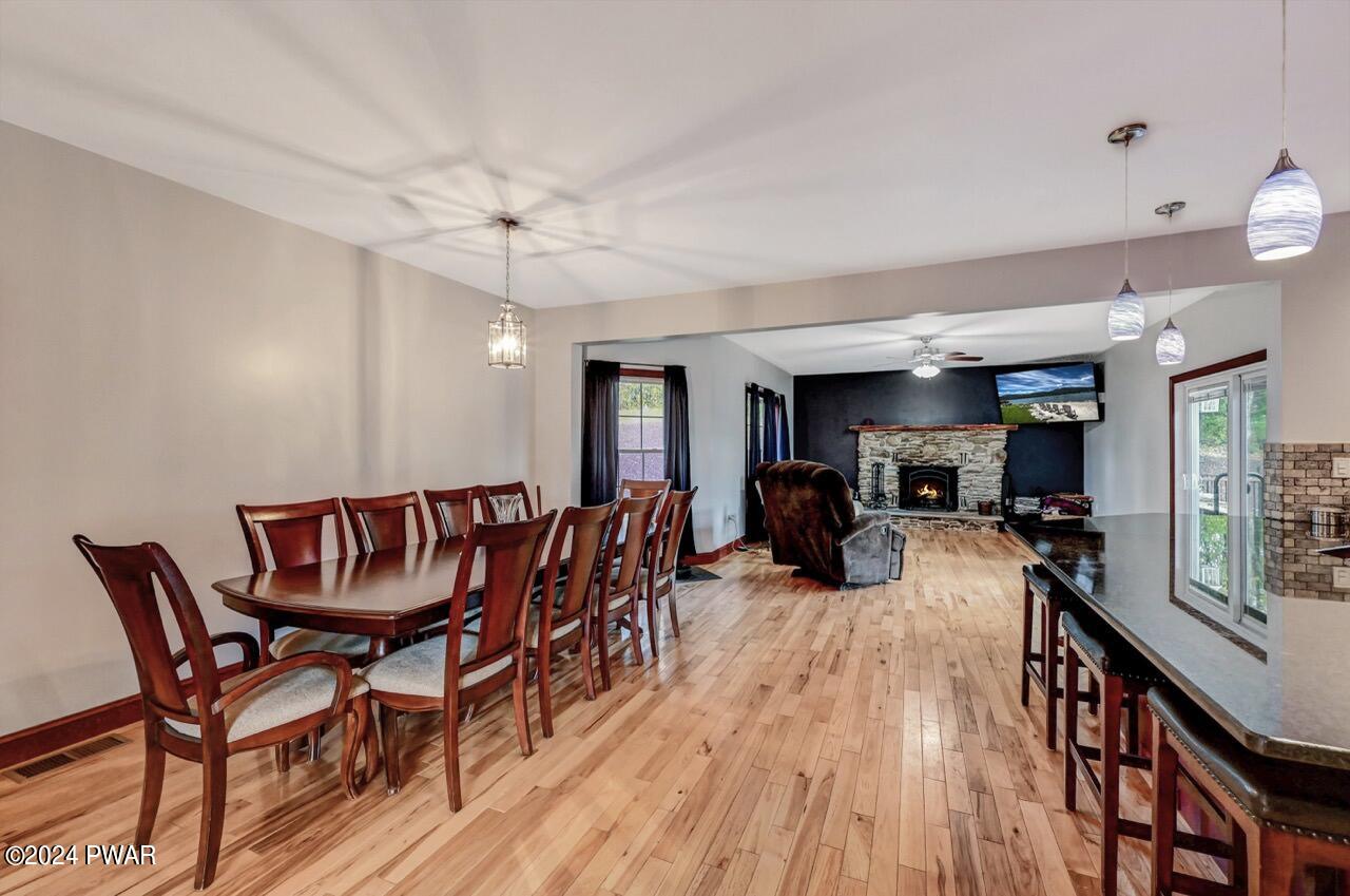 A dining area with a wooden table and chairs, looking into a living room with a stone fireplace and a kitchen counter with bar stools.