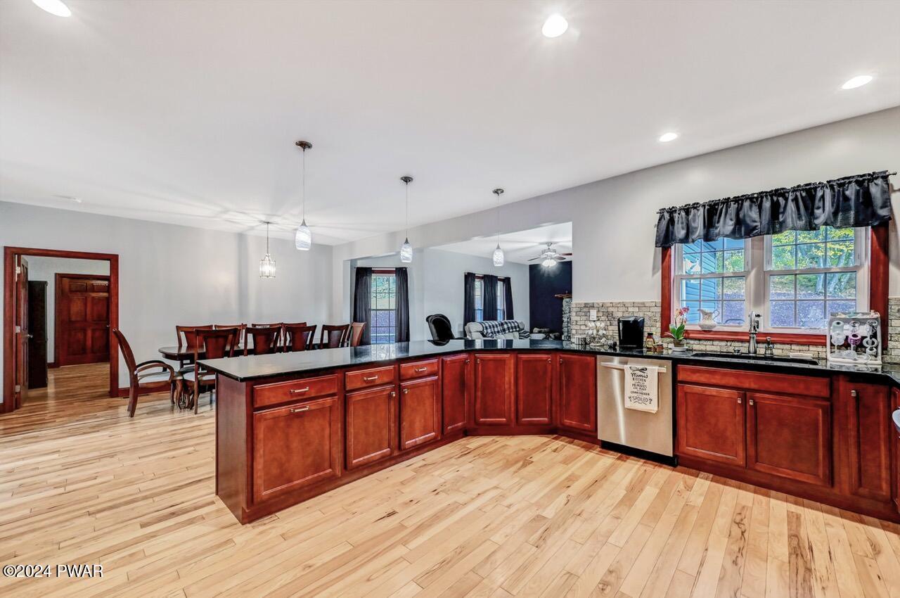 Open-concept kitchen with cherry cabinets, black countertops, a large island, hardwood floors, and a dining area in the background.