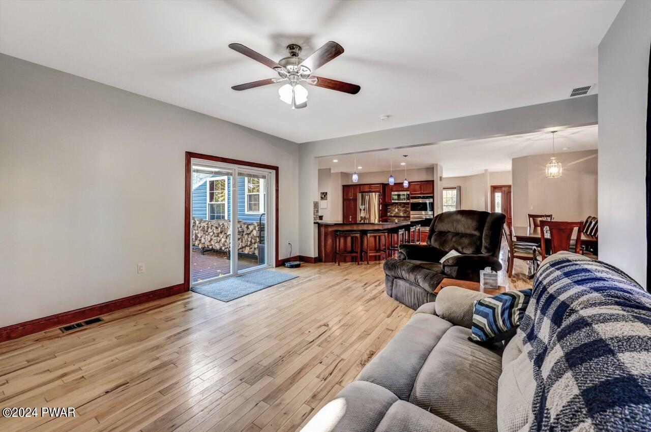 Open living room with hardwood floors, ceiling fan, sliding glass door to deck, and an open view into the kitchen and dining area.
