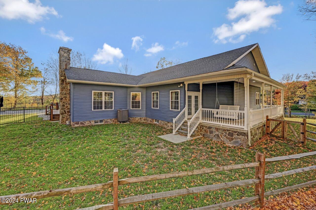 Exterior view of a blue house with a covered porch, stone chimney, fenced yard, and autumn trees.