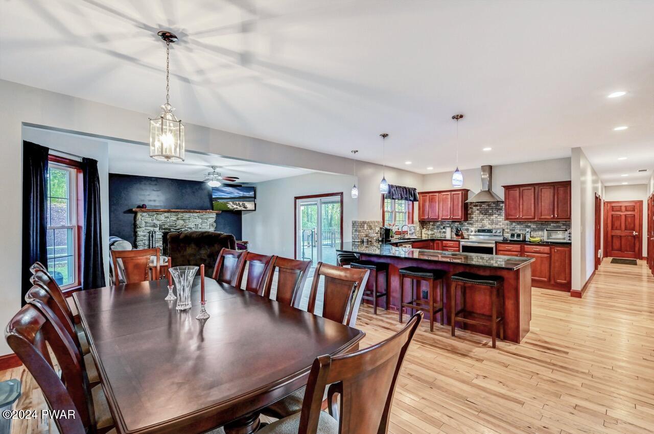 Open-concept kitchen with cherry cabinets, dark island, dining table in foreground, and a living area with stone fireplace in the background.