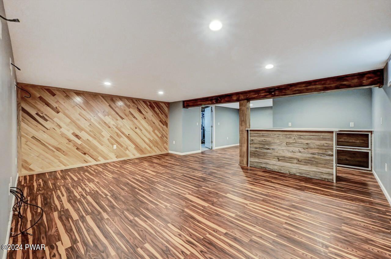 Finished basement recreation room with wood-look flooring, a wood accent wall, recessed lights, and a bar area.