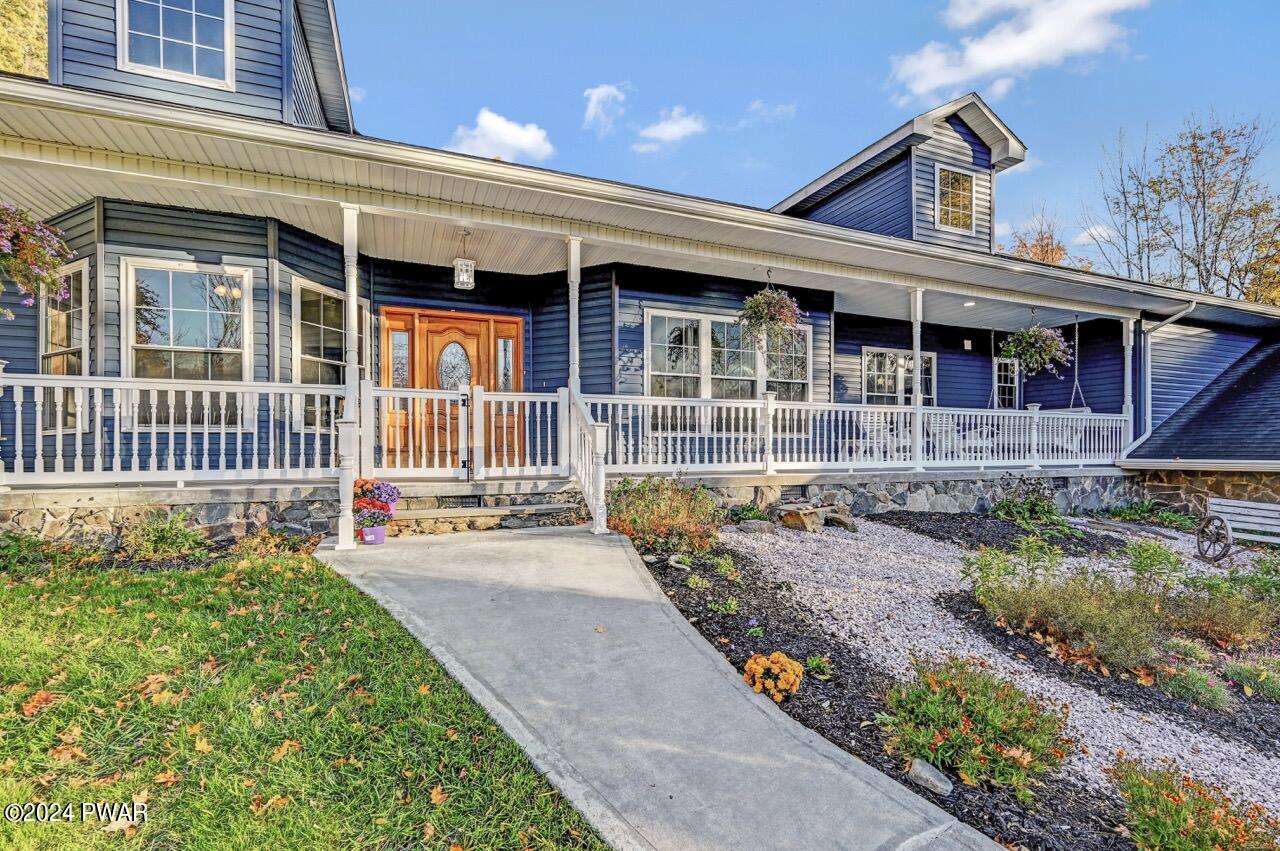 Front exterior of a blue house with a covered porch, white railings, a concrete walkway, and landscaped yard under a blue sky.