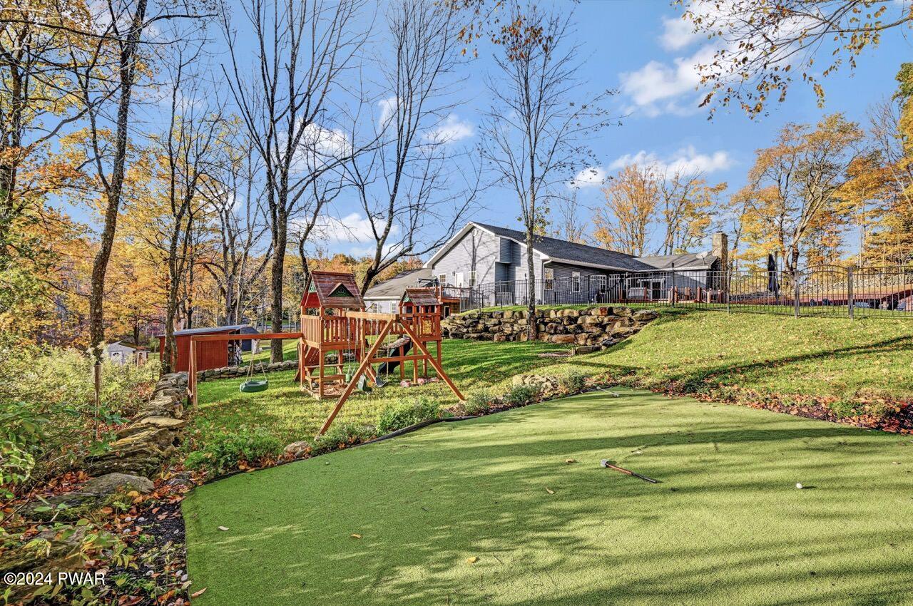 Landscaped backyard with a children’s playset, retaining wall, and a small putting green in front of a house.