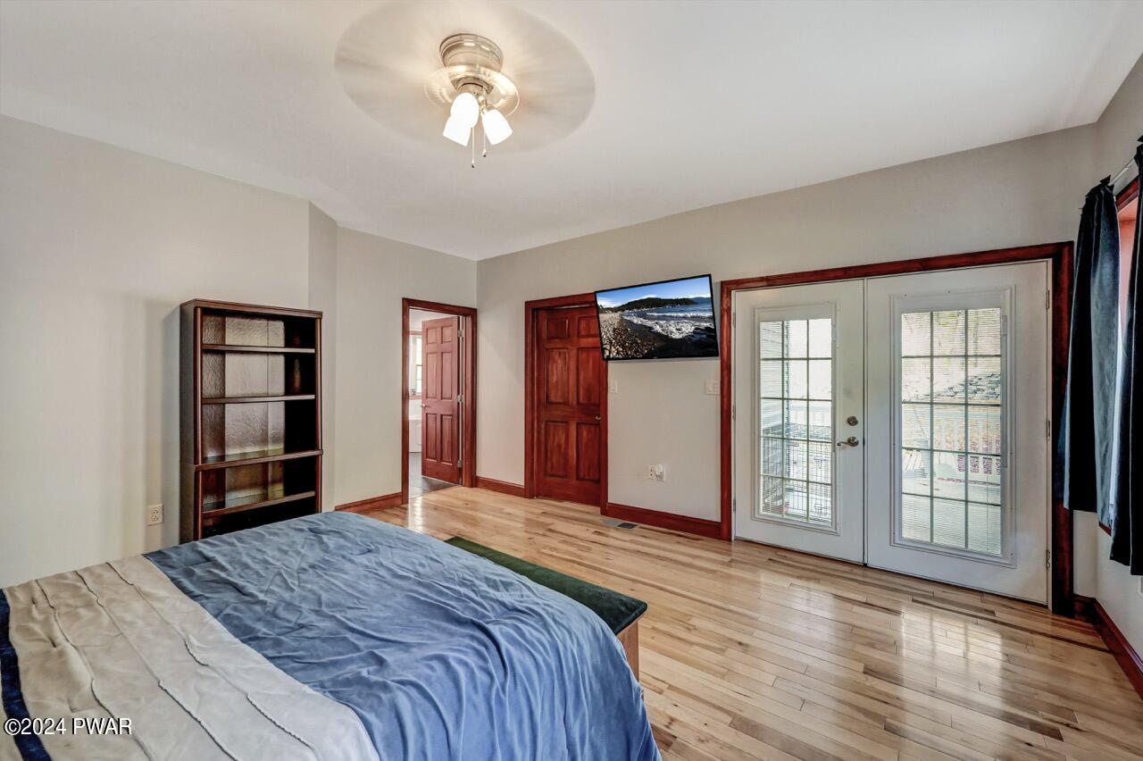 A bedroom with hardwood floors, a bed, bookshelf, ceiling fan, and French doors leading outside.
