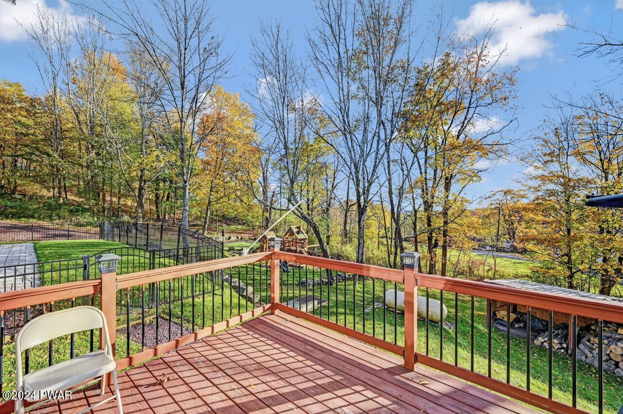 View from a wooden deck with a chair, overlooking a fenced grassy yard and trees in autumn.
