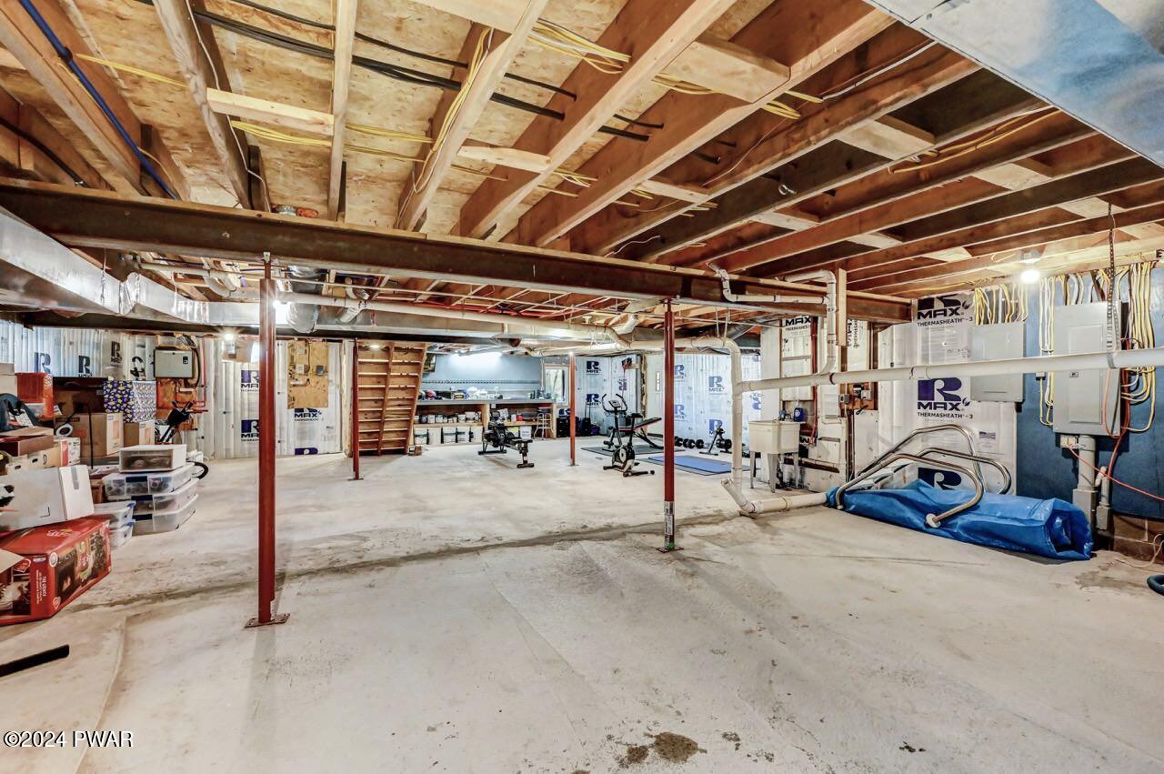 Unfinished basement with exposed ceiling joists, support posts, utility equipment, and storage items.