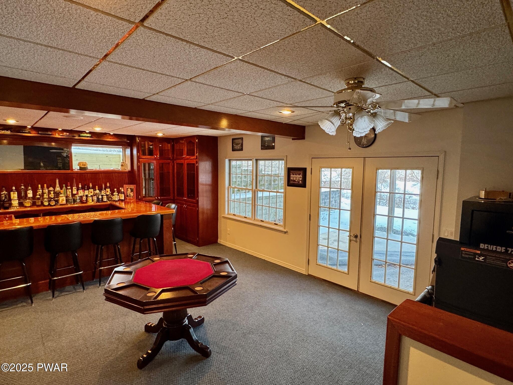 Finished basement room with a wet bar, barstools, poker table, French doors, and a ceiling fan.