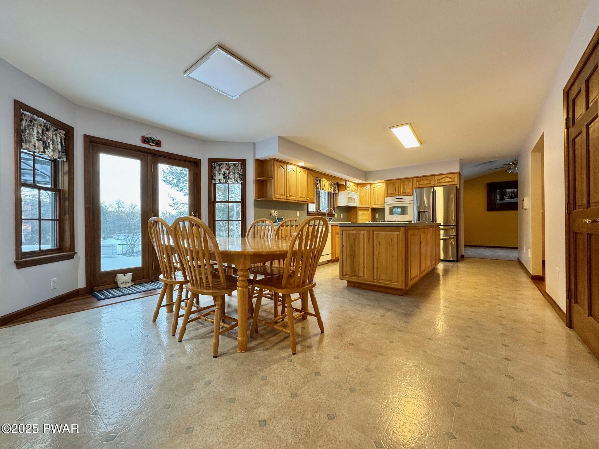 Open kitchen with wood cabinets, island, dining table, and adjacent dining area with glass door and windows.