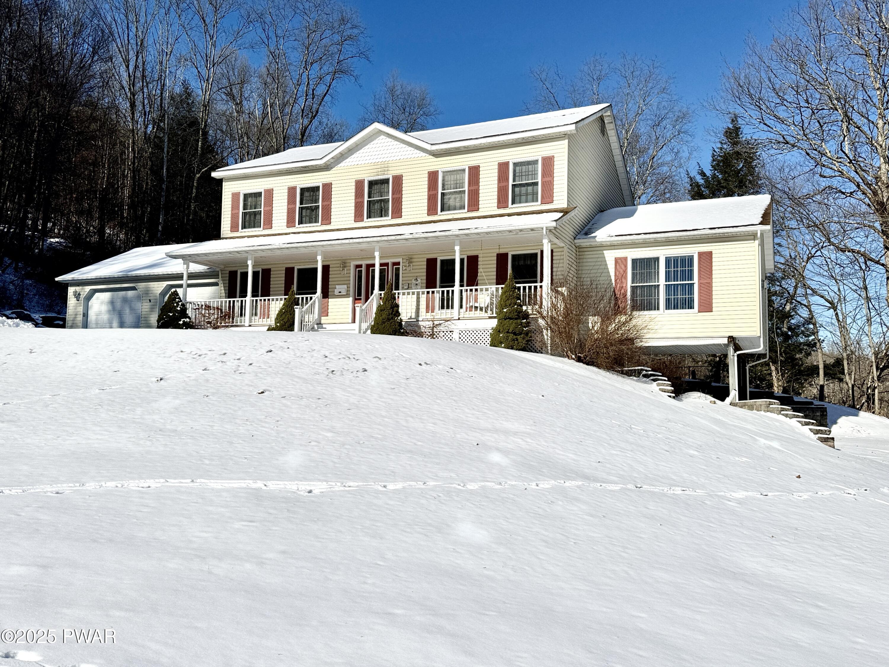 Front exterior of a two-story house with a garage, porch, and snow-covered yard under a clear blue sky.