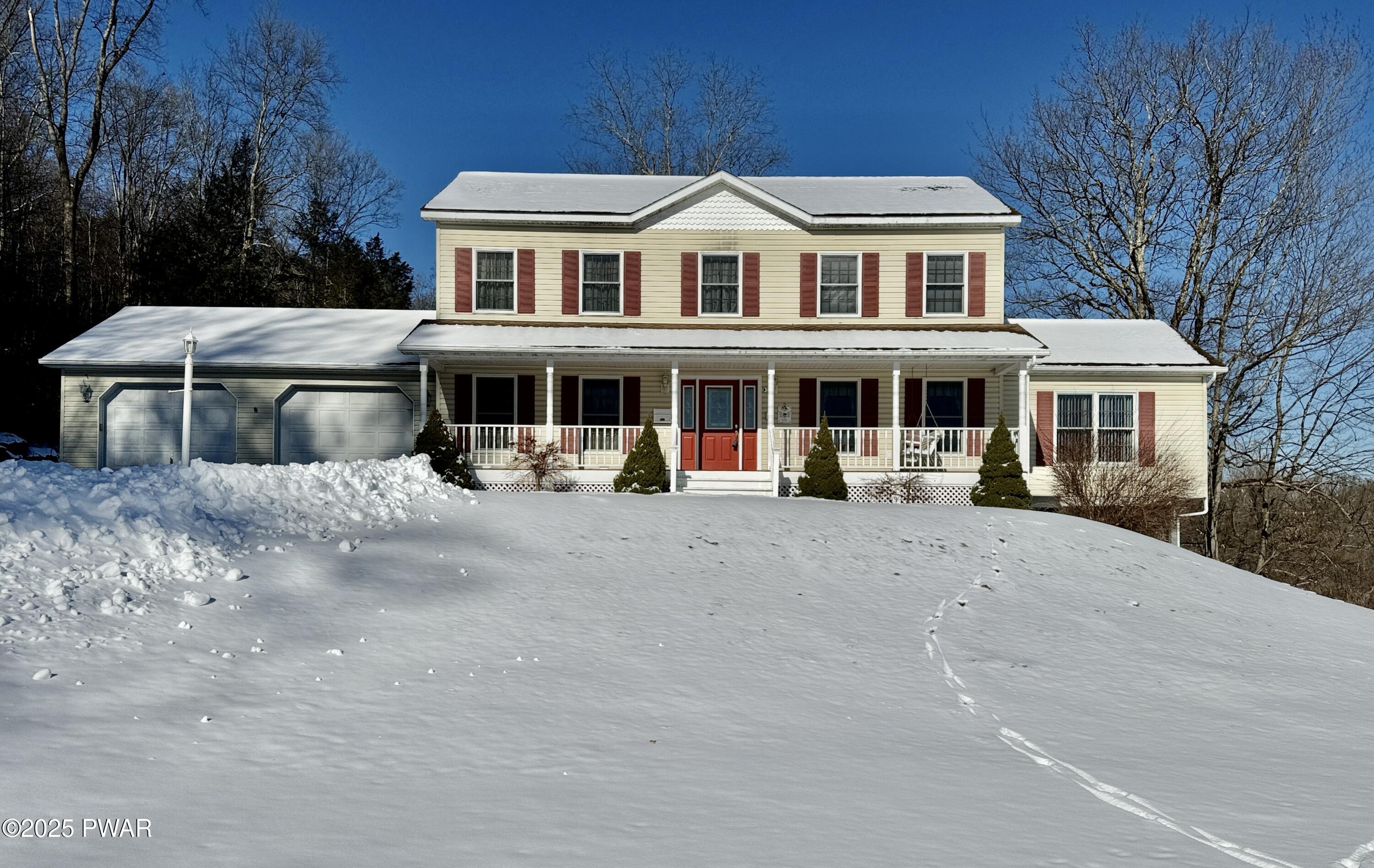 Front exterior of a two-story suburban house with attached garage, porch, and snow-covered lawn.
