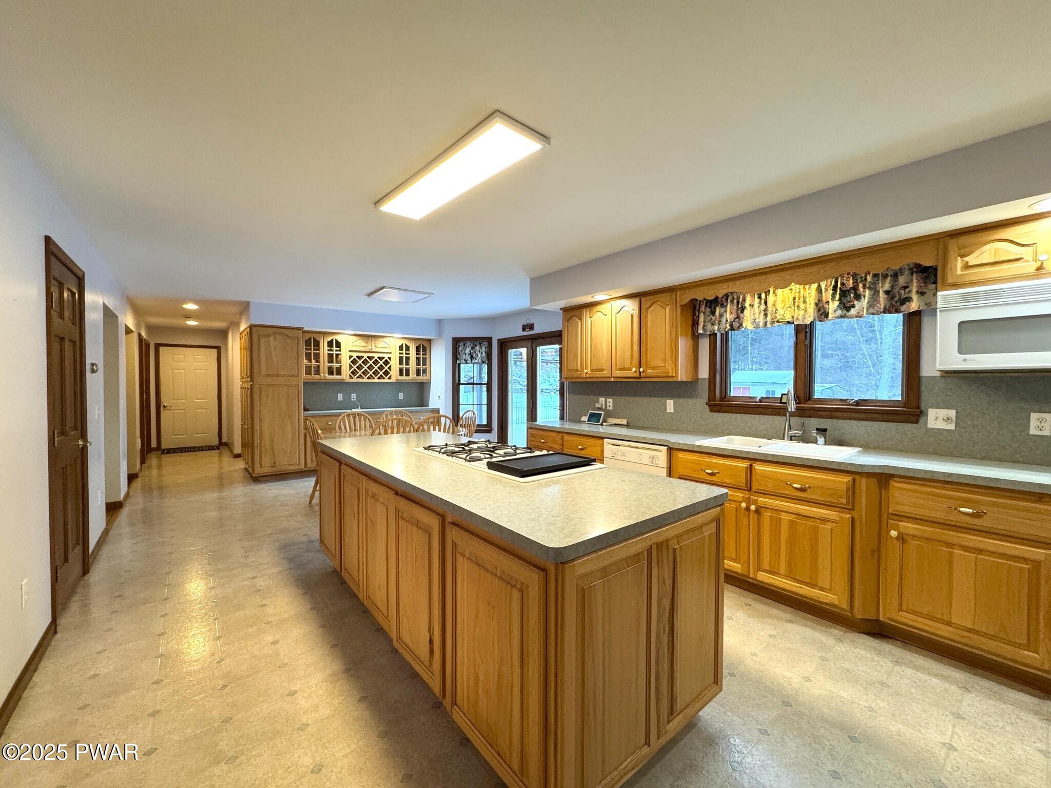 Spacious kitchen with wood cabinets, center island with cooktop, sink under windows, and an adjacent breakfast area.