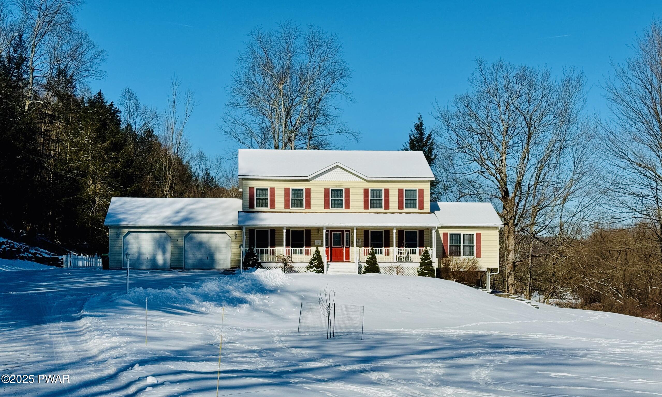 Front exterior of a two-story house with a covered porch, attached garage, and snow-covered yard under a clear blue sky.