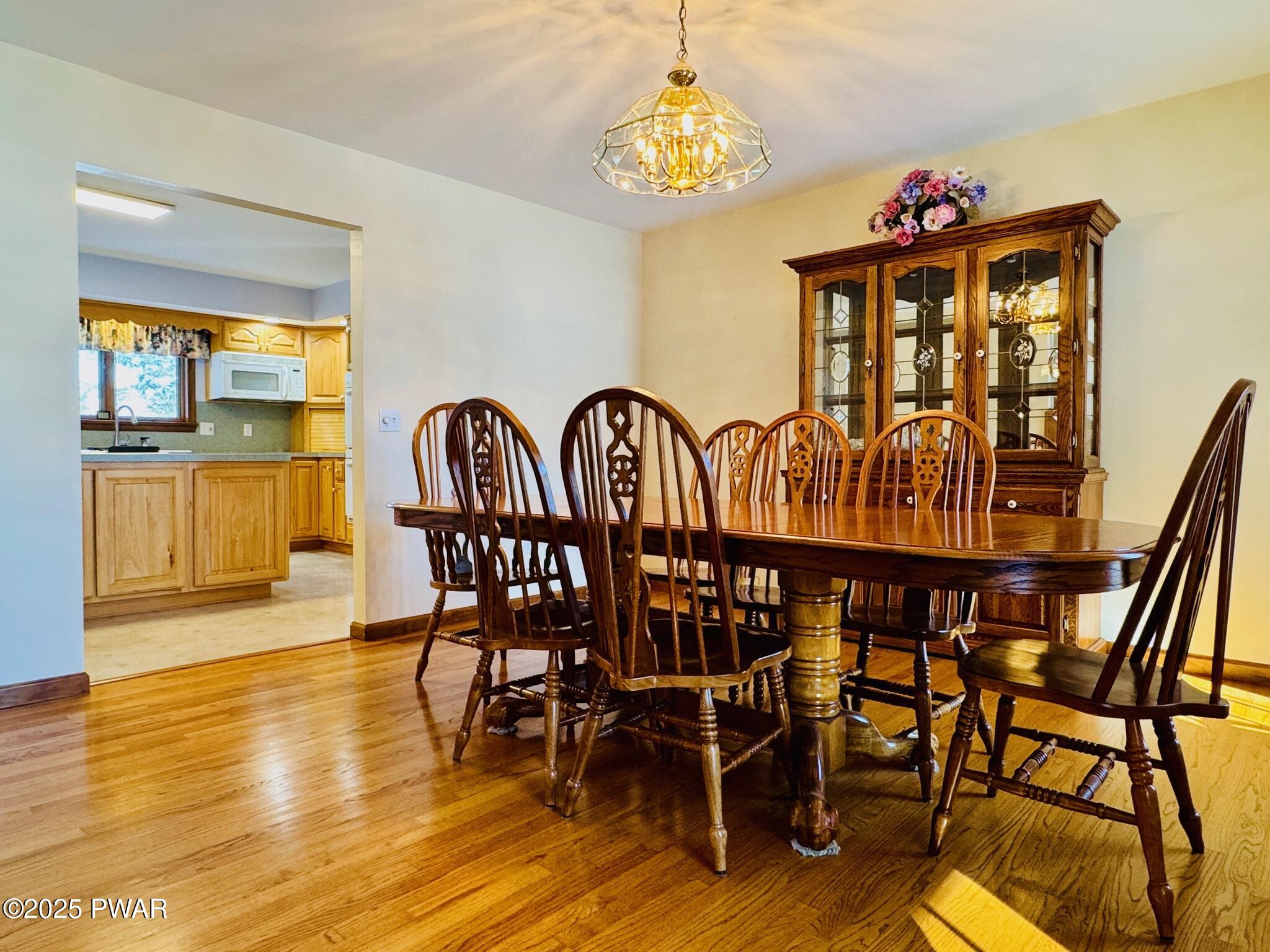 Formal dining room with a wooden dining table and chairs, china cabinet, hardwood floor, and a view into the kitchen through a wide doorway.