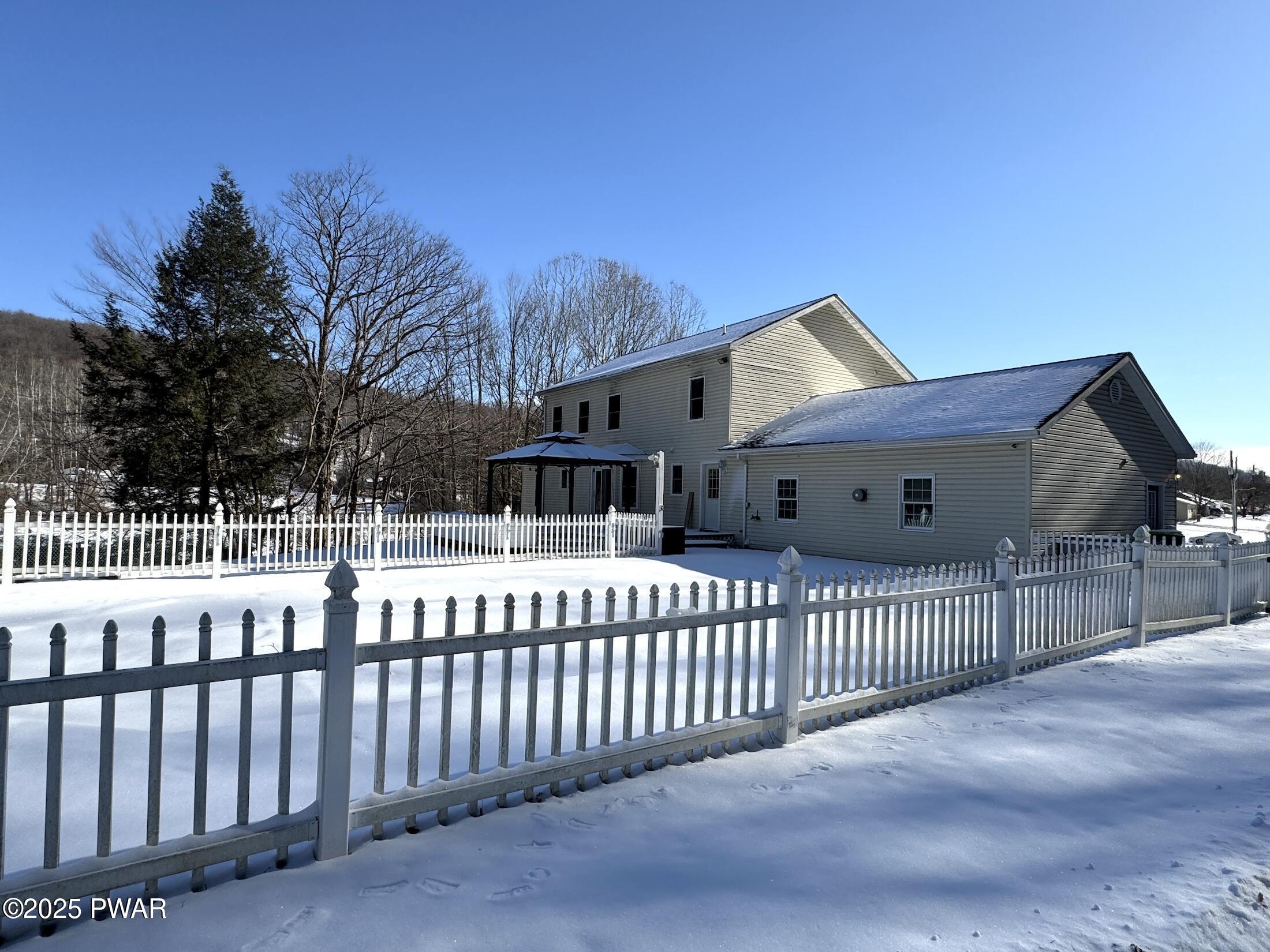 Snow-covered suburban house with white picket fence under a clear blue sky.
