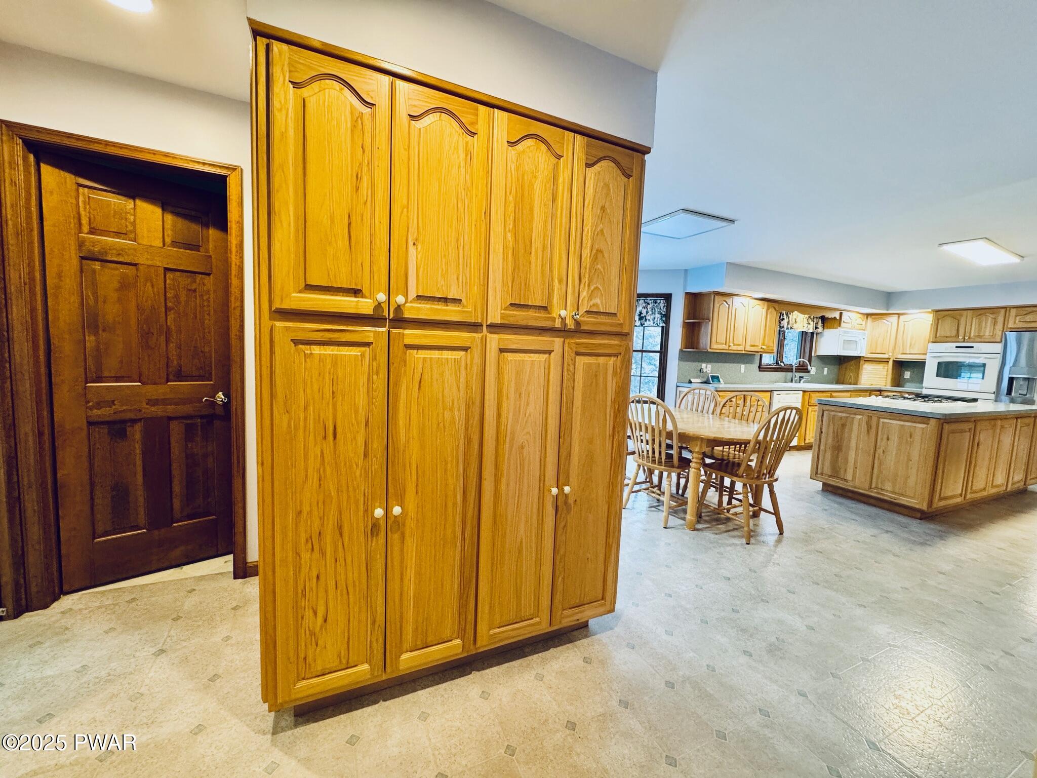 Kitchen with wood cabinets, a center island, dining table, and visible appliances including a refrigerator and wall oven.