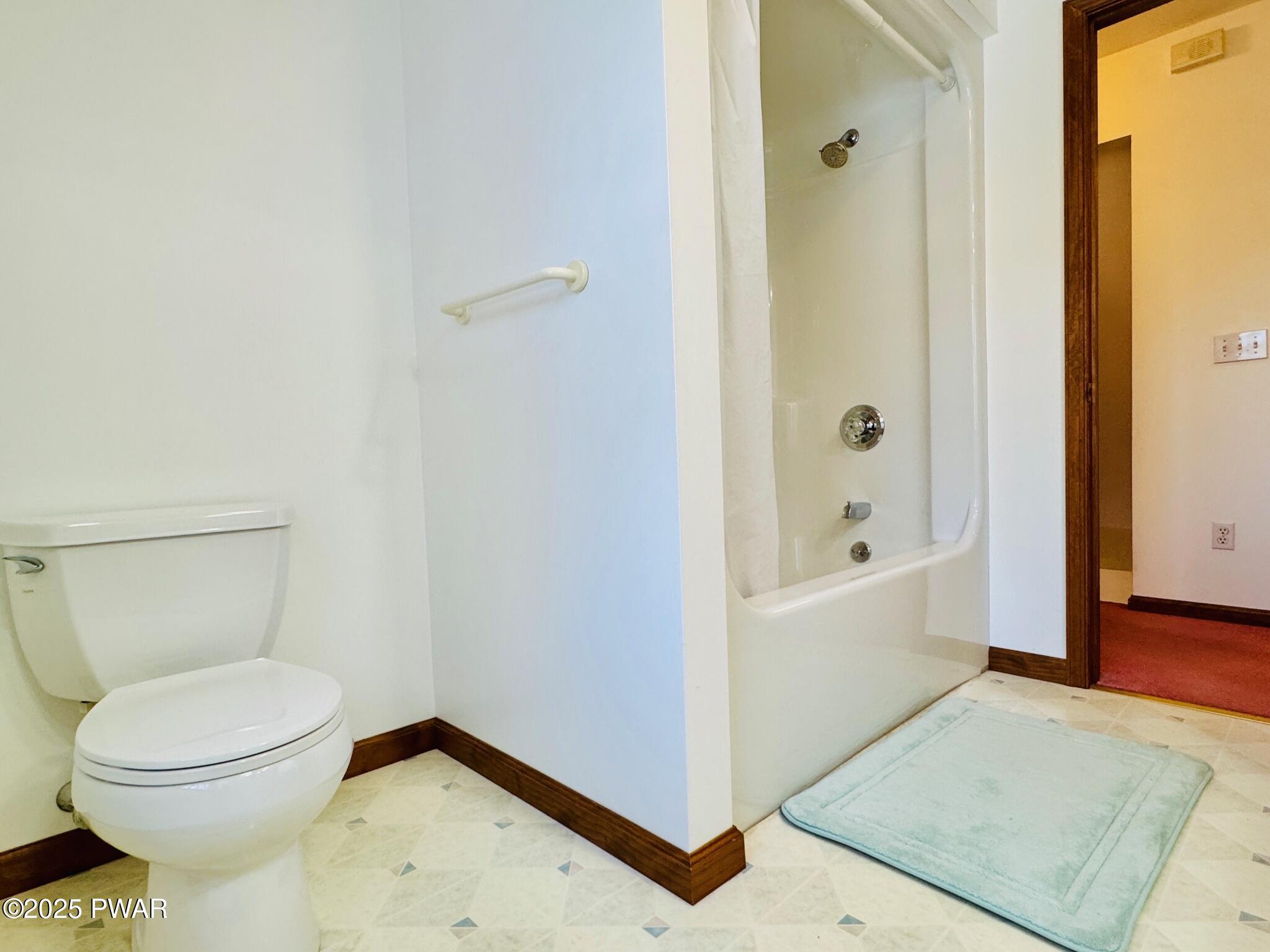 Bathroom with a toilet, walk-in shower or tub area, towel bar, and bath mat near an open doorway.