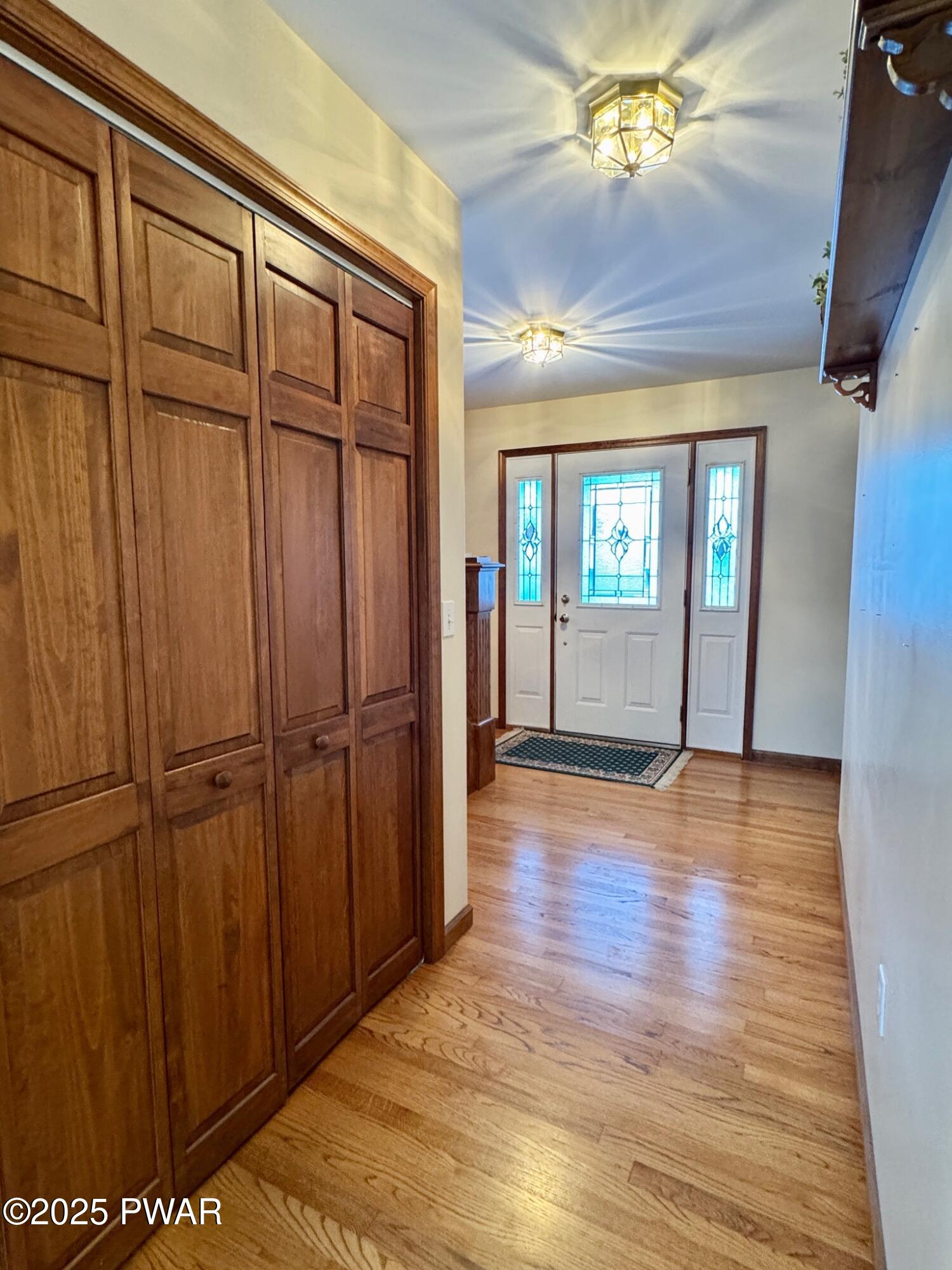 Interior entry hall with hardwood floors, a large wood closet on the left, and a front door with decorative glass sidelights and transom.