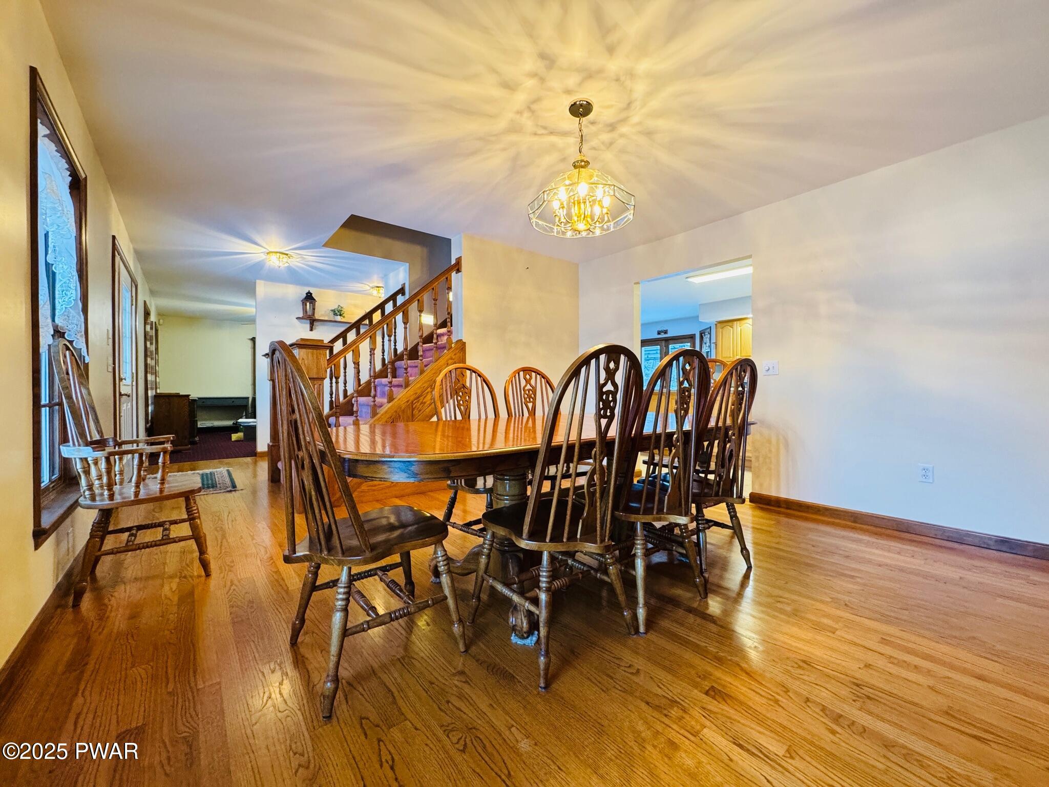 Dining room with hardwood floors, a wooden dining table and chairs, staircase in the background, and a doorway into the kitchen.