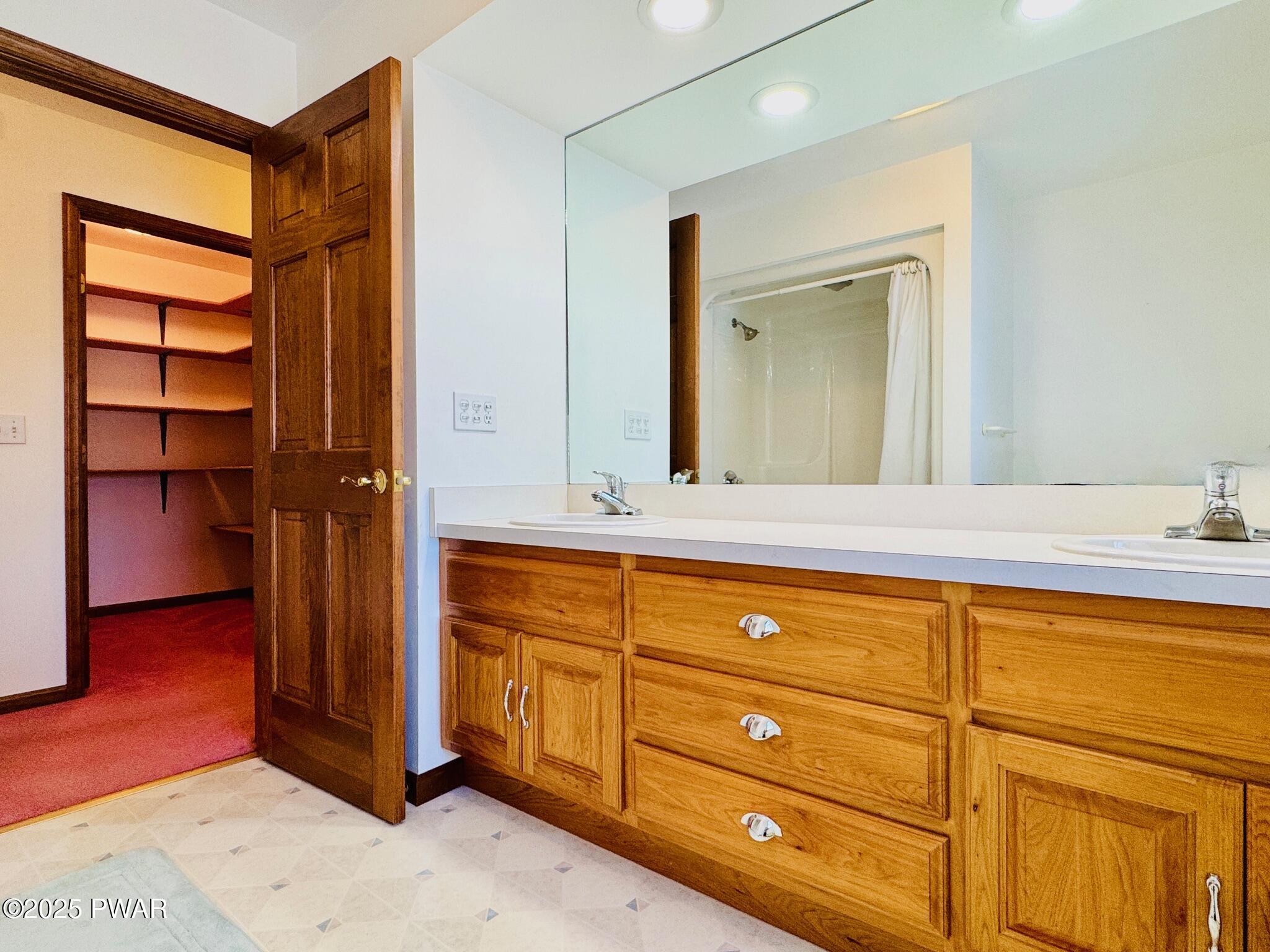 Bathroom with wooden double-sink vanity, large mirror, and an open closet doorway beside it.