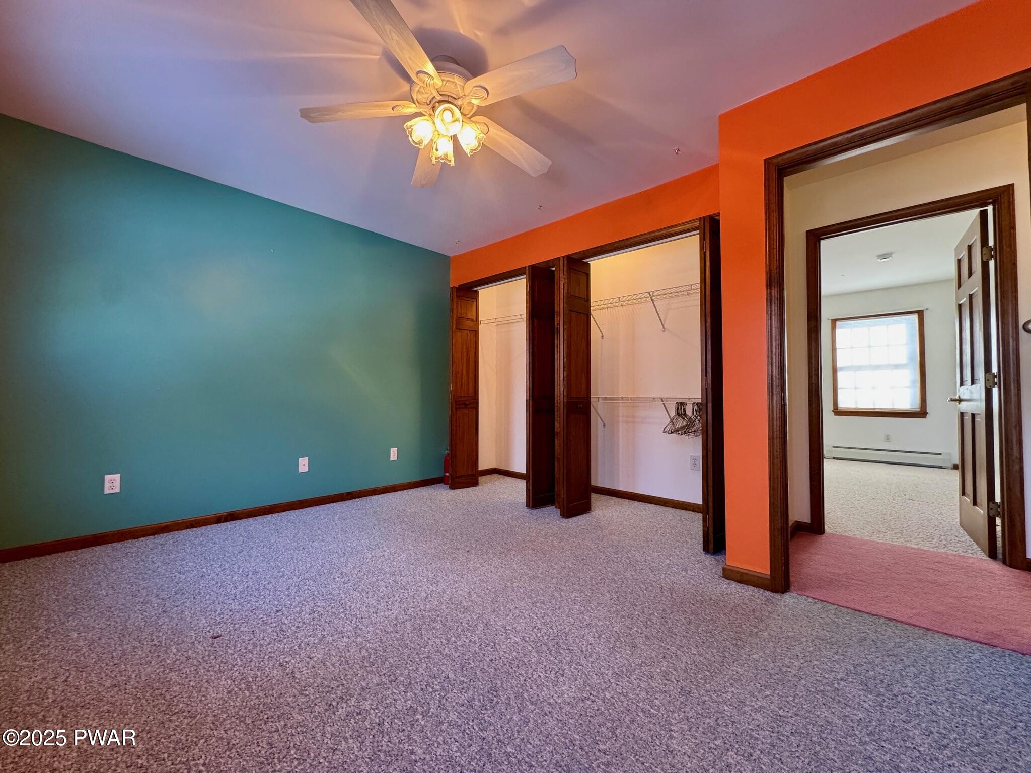 Empty bedroom with colorful painted walls, carpet, ceiling fan, and walk-in closet openings leading to an adjacent room.