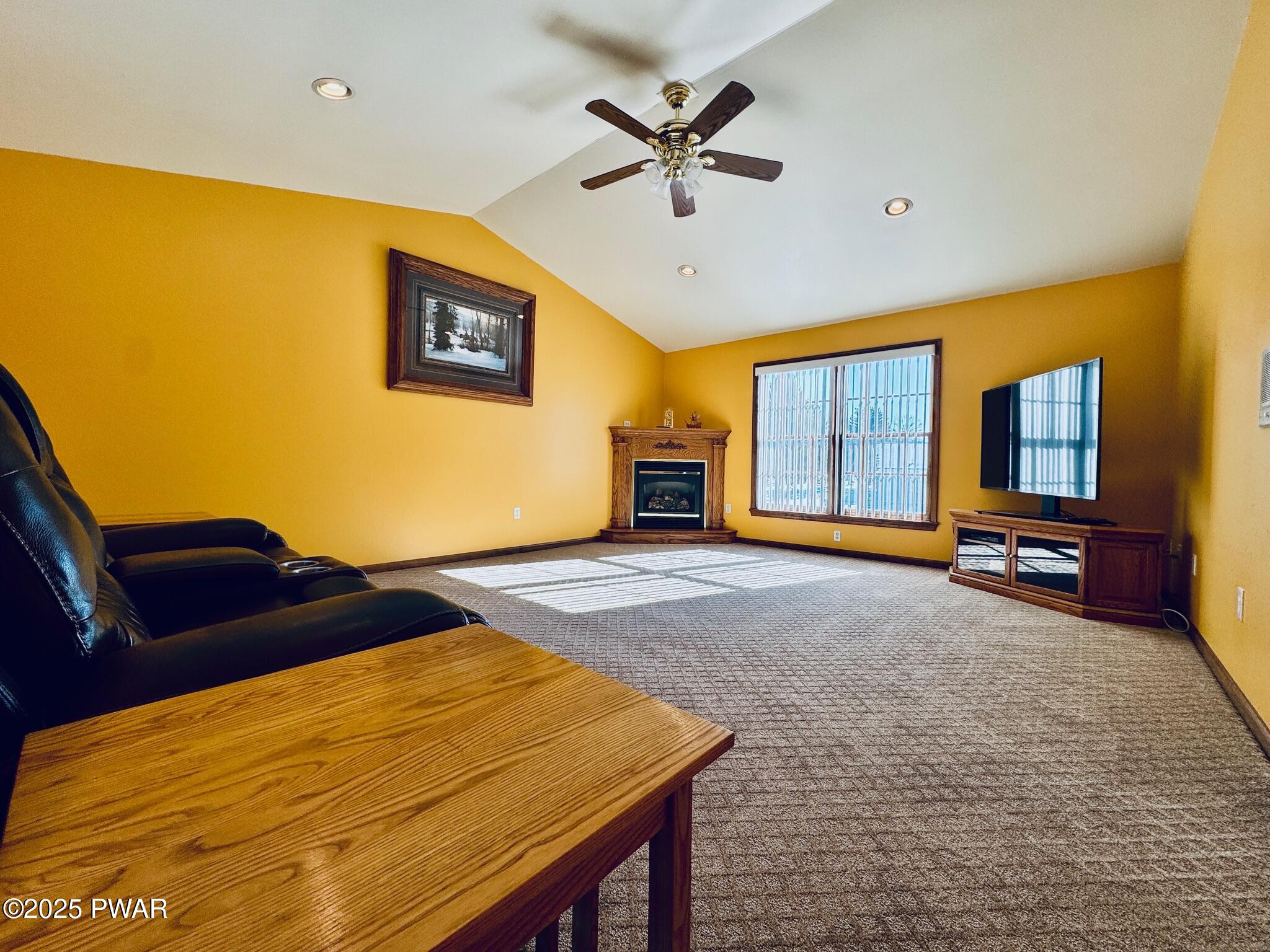 Living room with yellow walls, vaulted ceiling, ceiling fan, fireplace, large window, TV, and leather recliner seating.