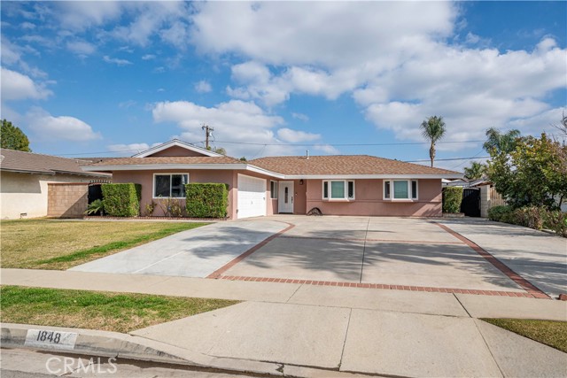 Single-story ranch-style home with a broad concrete driveway, low front lawn, and blue sky.