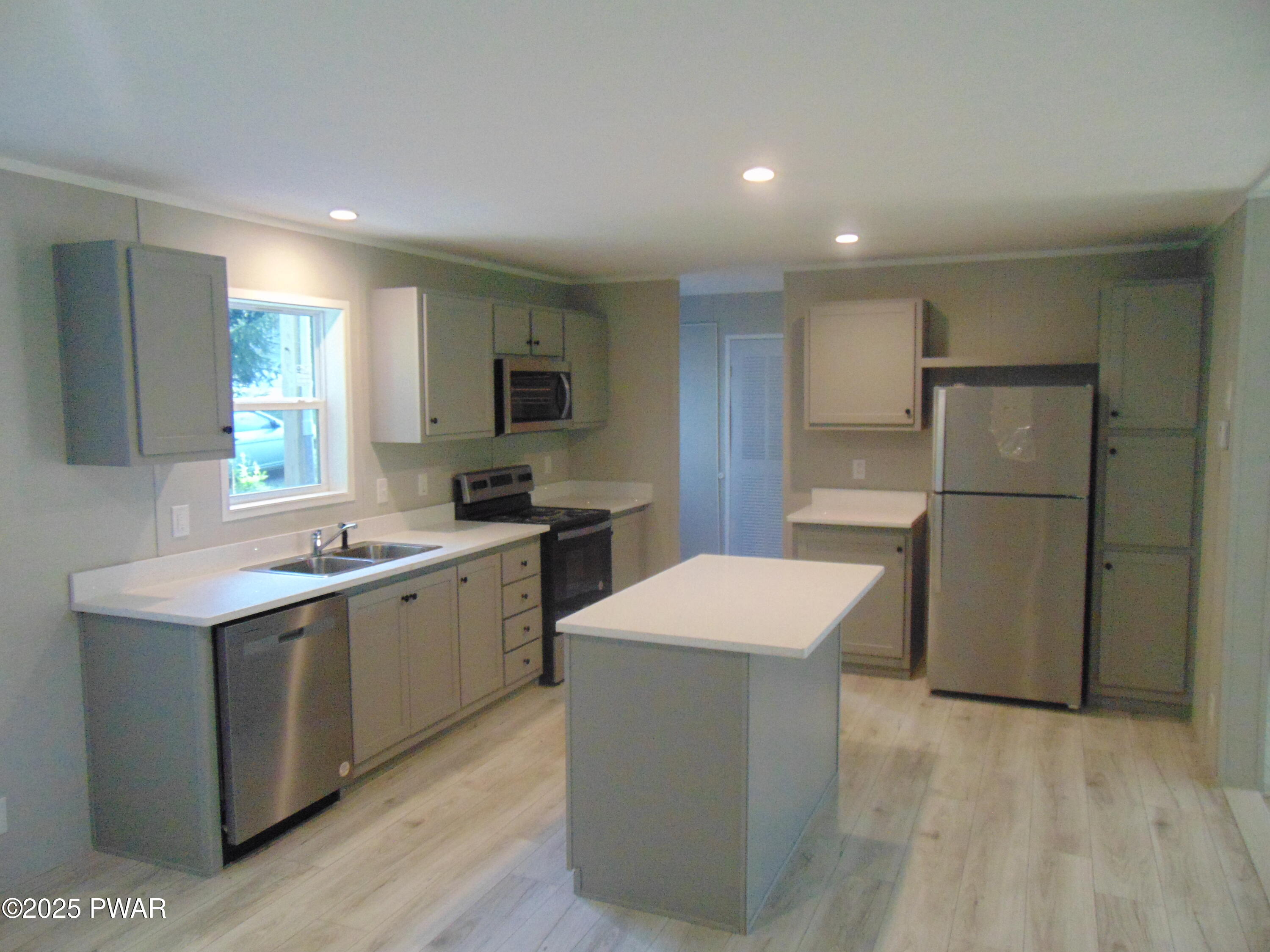 Modern kitchen with central island, stainless steel refrigerator and dishwasher, white countertops, gray cabinets, and recessed lighting.