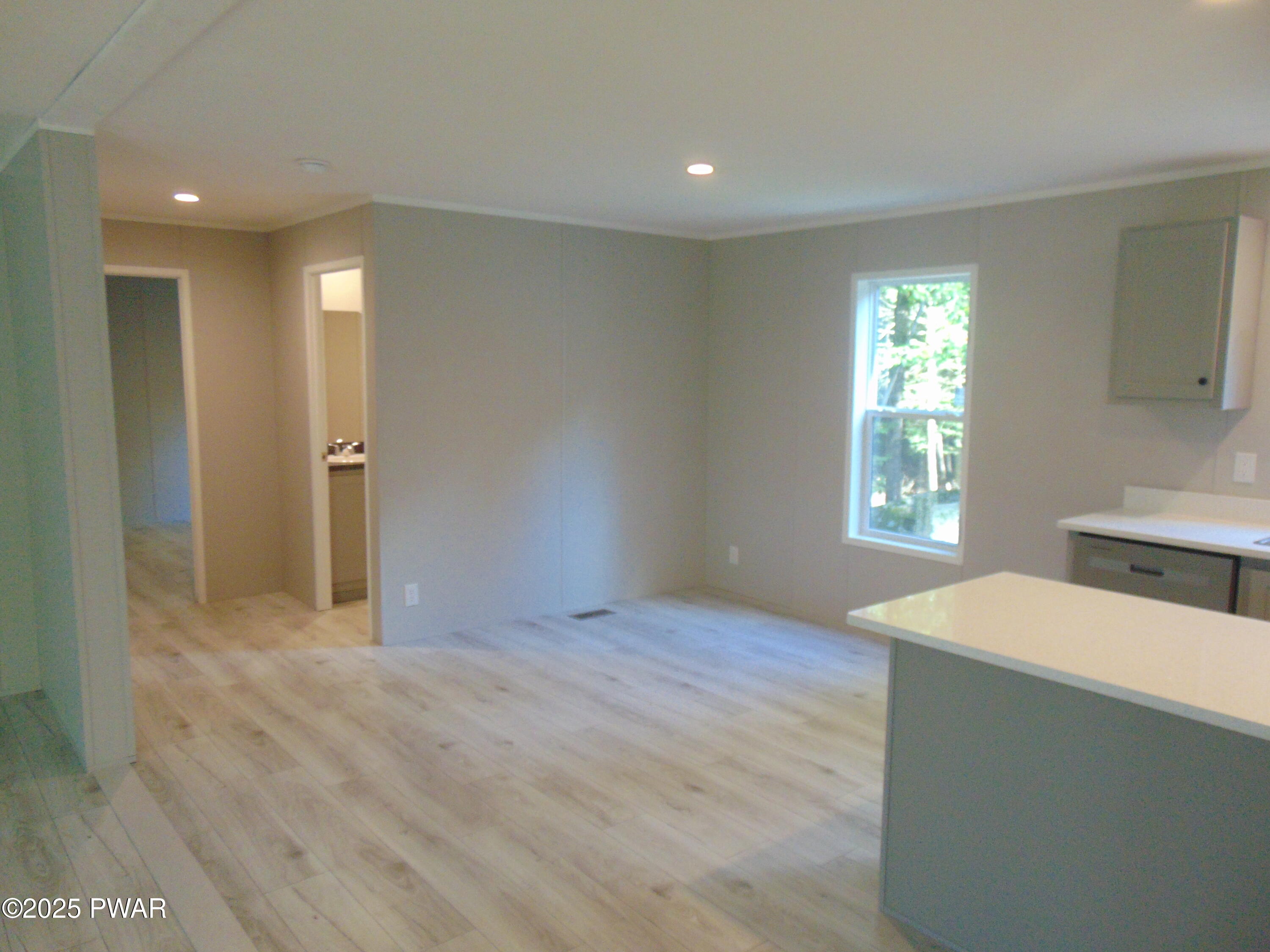 Empty kitchen area with light wood floors, gray walls, white countertops, a window, and doorways to adjacent rooms.