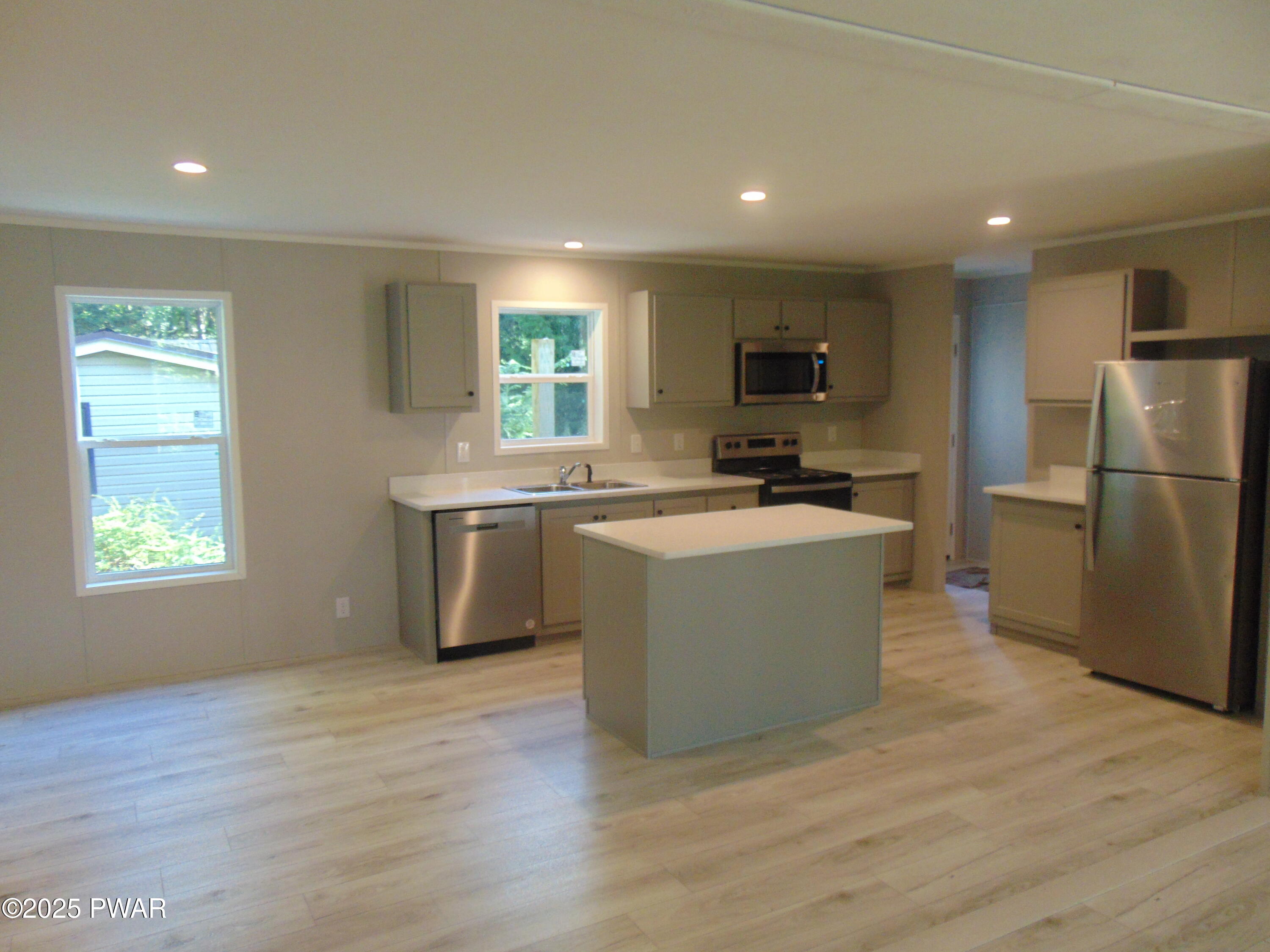 Modern kitchen with a center island, stainless steel refrigerator and appliances, light cabinetry, and wood-look flooring.