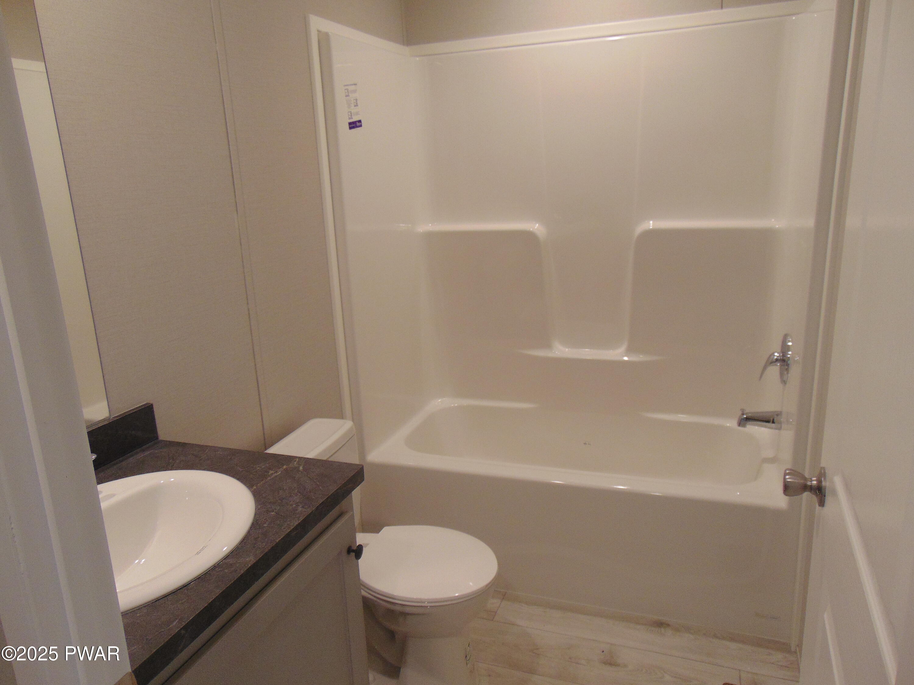 Small bathroom with a white tub-shower surround, toilet, and vanity with a round sink and dark countertop.