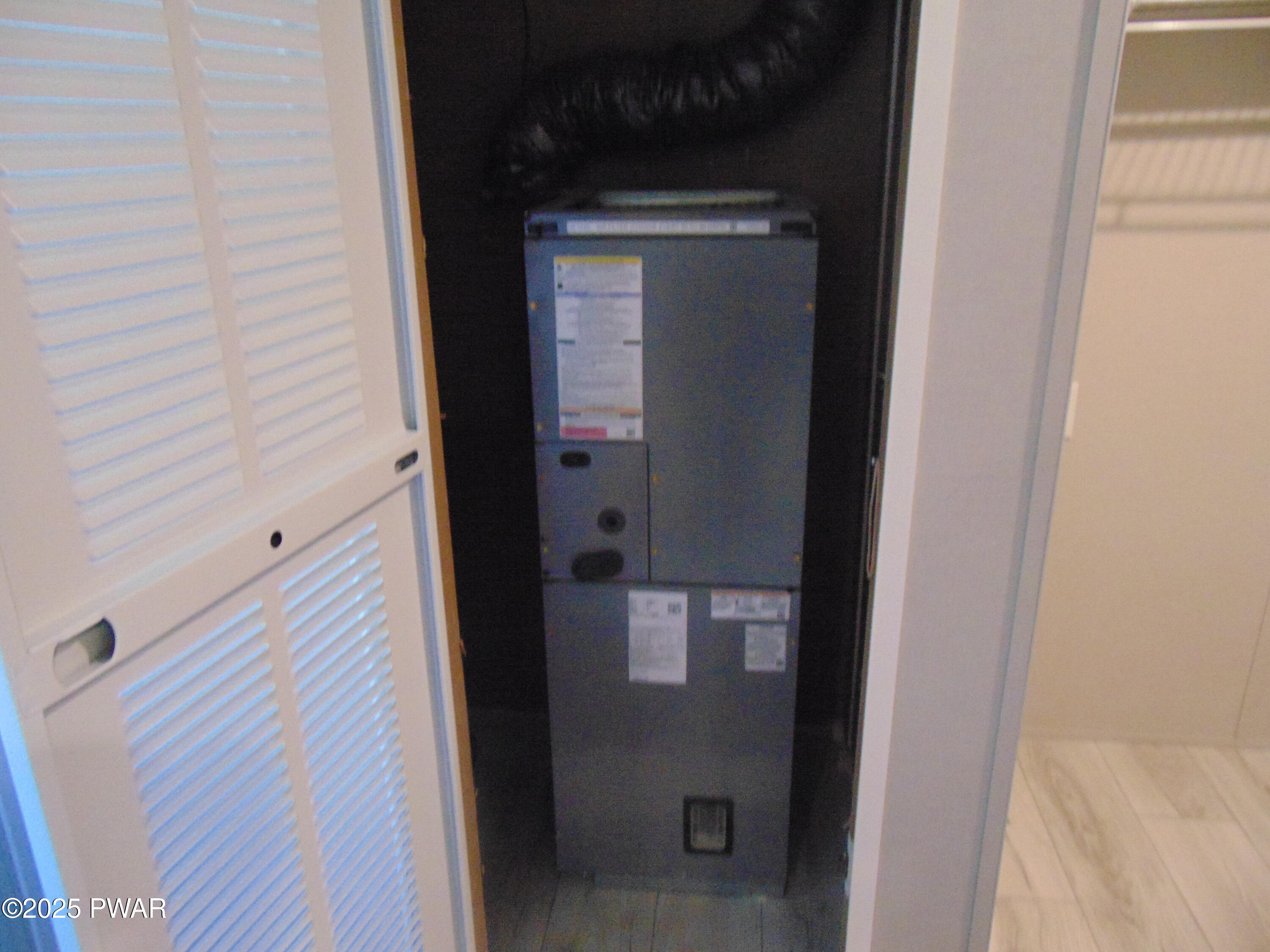 Open utility closet showing a large HVAC air handler unit inside, with louvered closet doors and adjacent tiled hallway or laundry area.