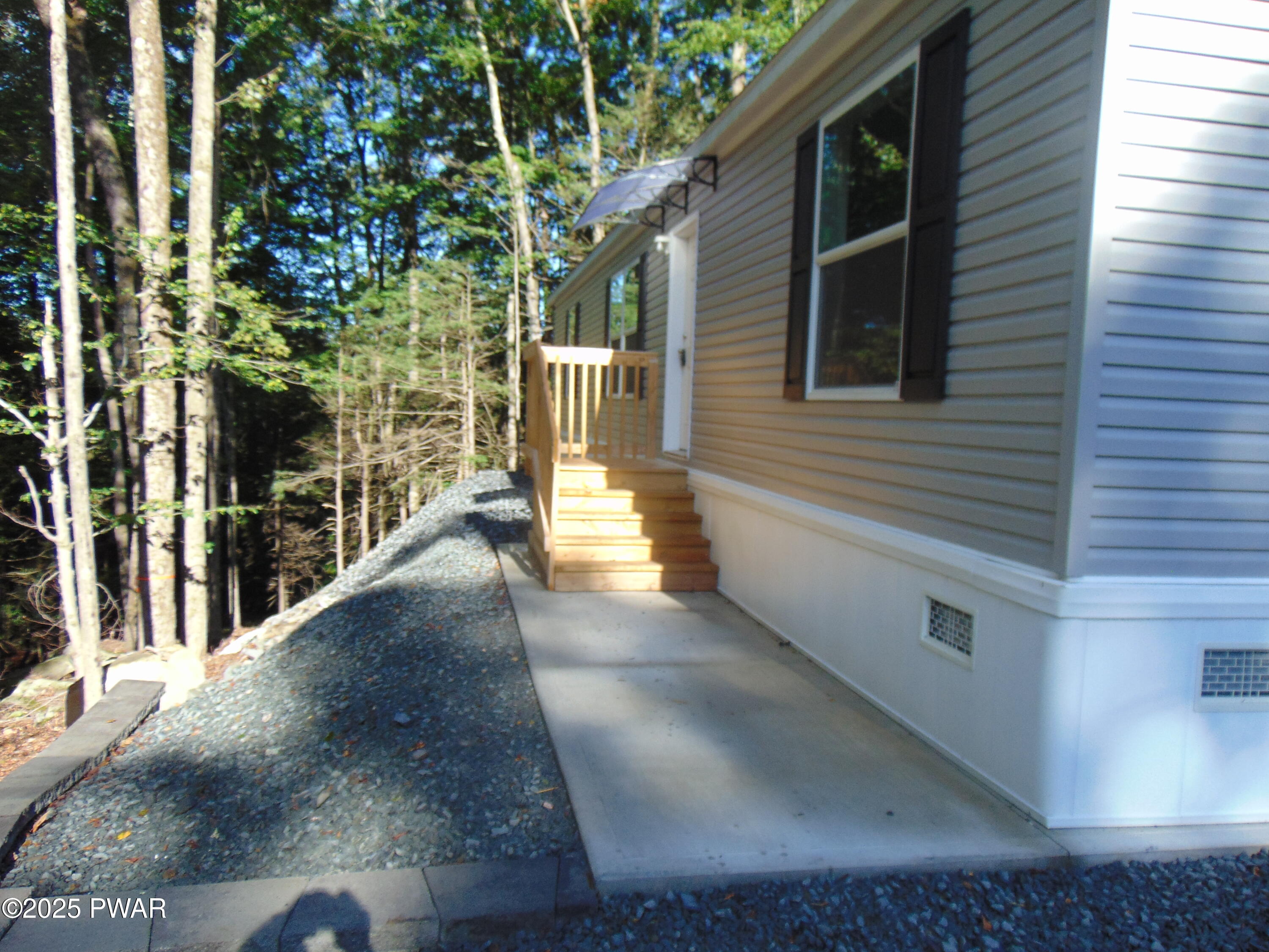 Side and back exterior of a house with vinyl siding, a small stair landing, concrete walkway, and trees close to the home.