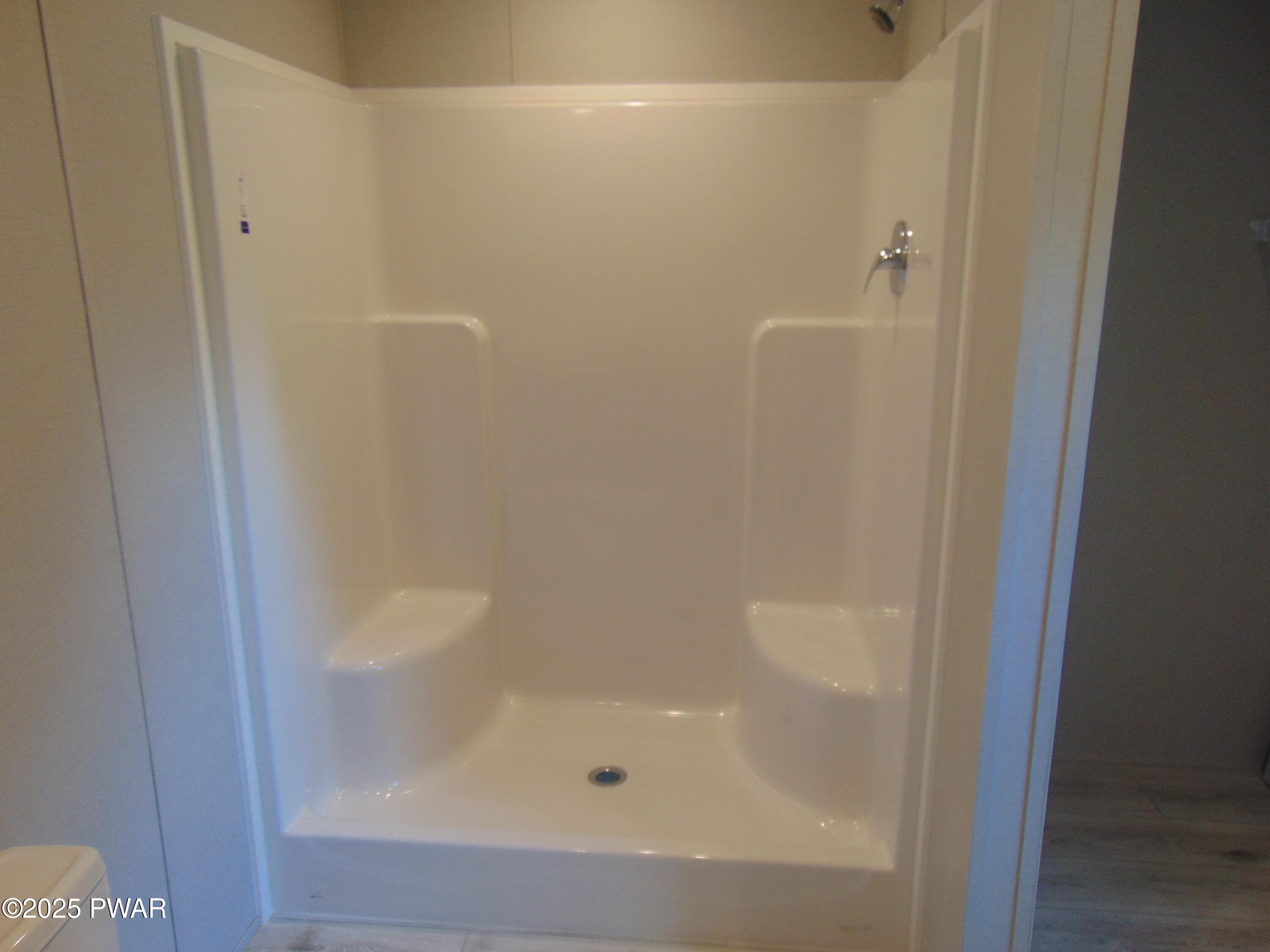 Empty bathroom shower stall with white surround and chrome handle.
