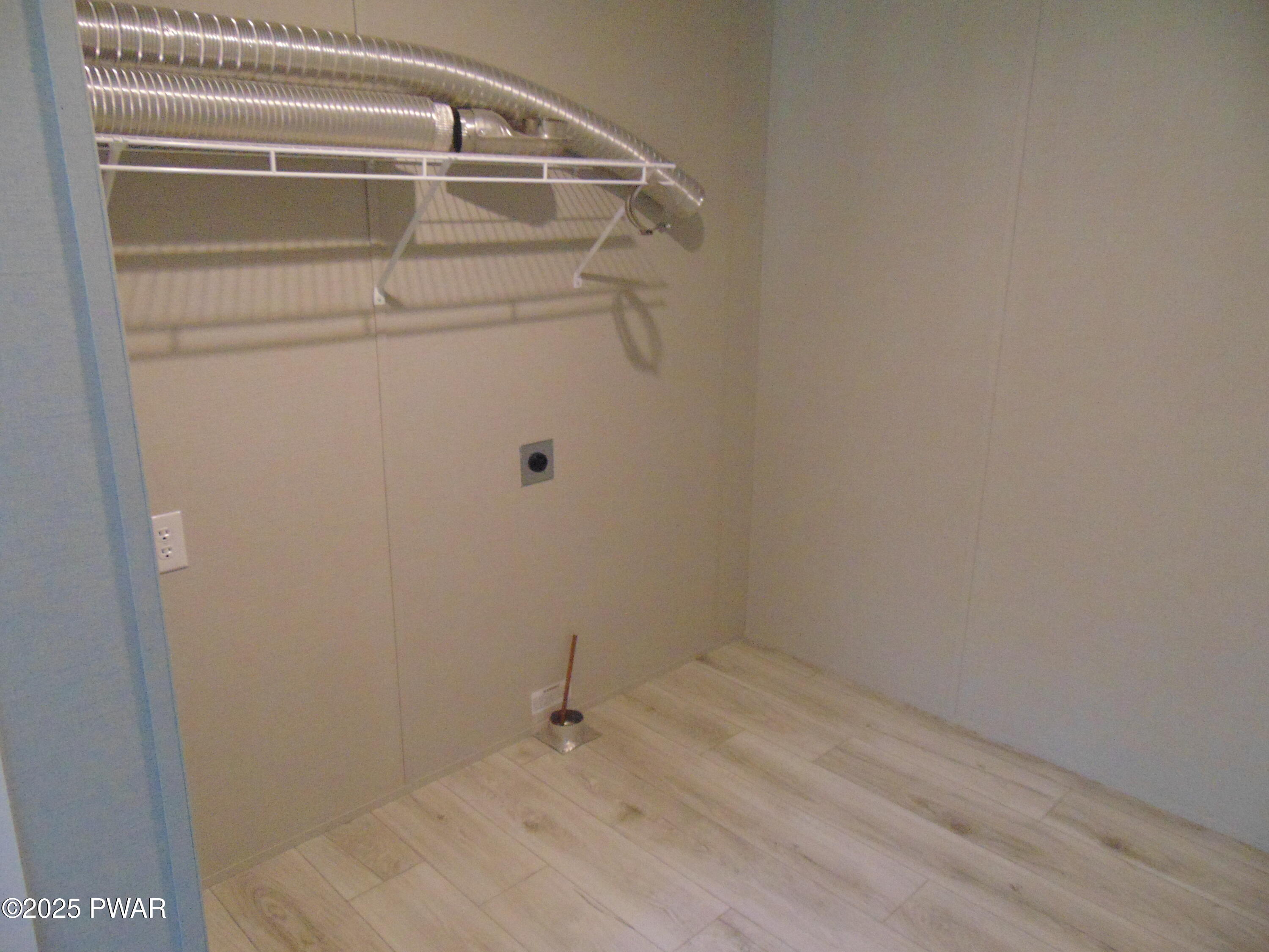 An empty walk-in closet with light wood flooring, white walls, a wire shelf and hanging rod, and exposed ventilation ducts near the ceiling.
