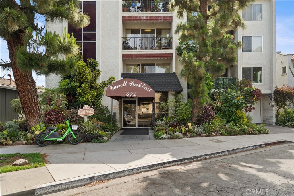 Street view of the Carroll Park East apartment building at 372 Carroll Avenue, with a landscaped entrance, balconies, and a bicycle outside.