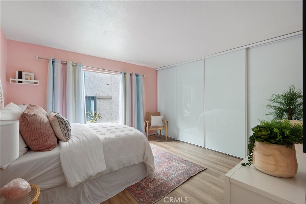 Bedroom at 372 Carroll E 201 with a bed against a pink wall, a large sliding-door wardrobe, a patterned rug, and potted greenery.