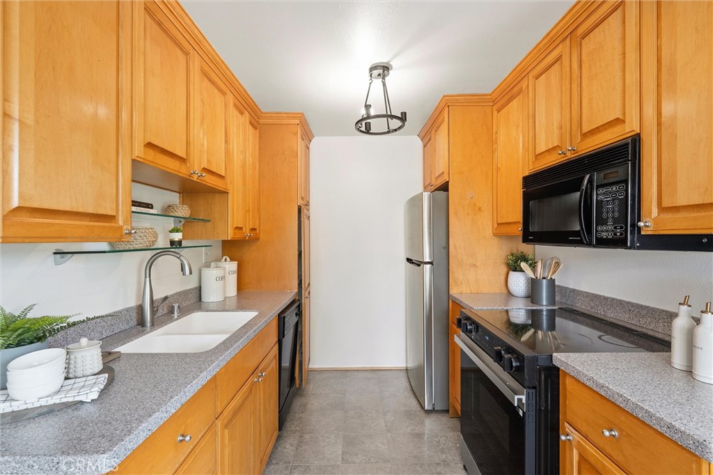 Galley kitchen at 372 Carroll E 201 with honey-colored wood cabinets, gray countertops, a stainless steel refrigerator, and a double-basin sink.