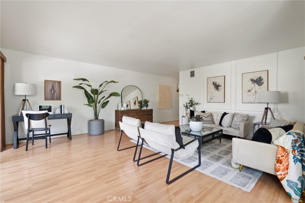Bright living room at 372 Carroll E 201 with light wood floors, a white sectional and lounge chairs around a glass coffee table, plus a desk and houseplants.