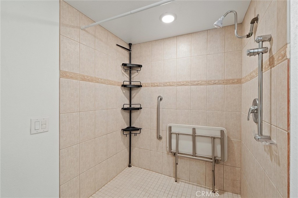 Tiled walk-in shower with a handheld showerhead, corner shelves, grab bars, and a fold-down seat in 372 Carroll E 201.